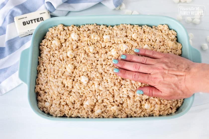 Pressing Rice Krispie treats into pan with hand.