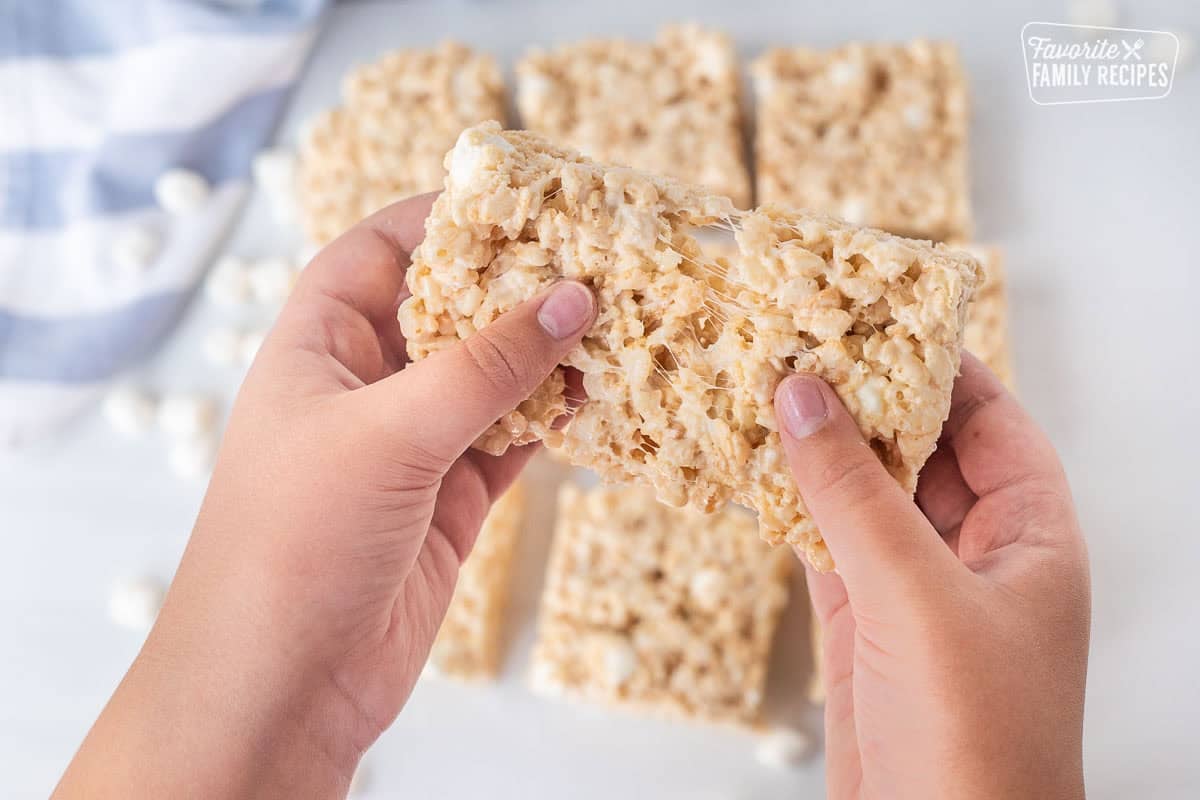 This Rice Krispie Treat recipe is foolproof! They never come out hard or dry, and it is less mess than making them over the stove! Hands pulling apart a microwave Rice Krispie treat.