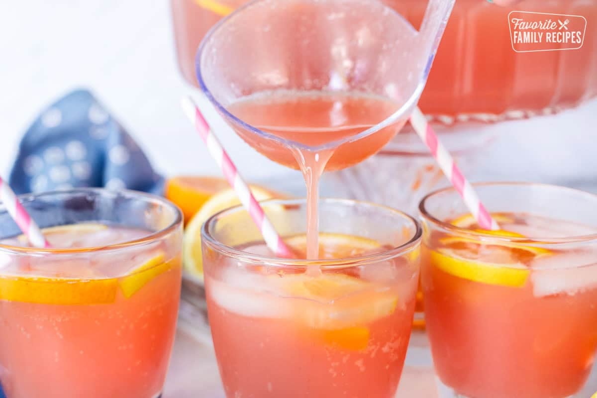 Ladle pouring party punch into glasses with fresh slices of oranges and lemons on top.