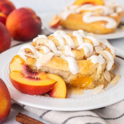 Peach cinnamon roll on a plate with sliced peaches and fork on the side.