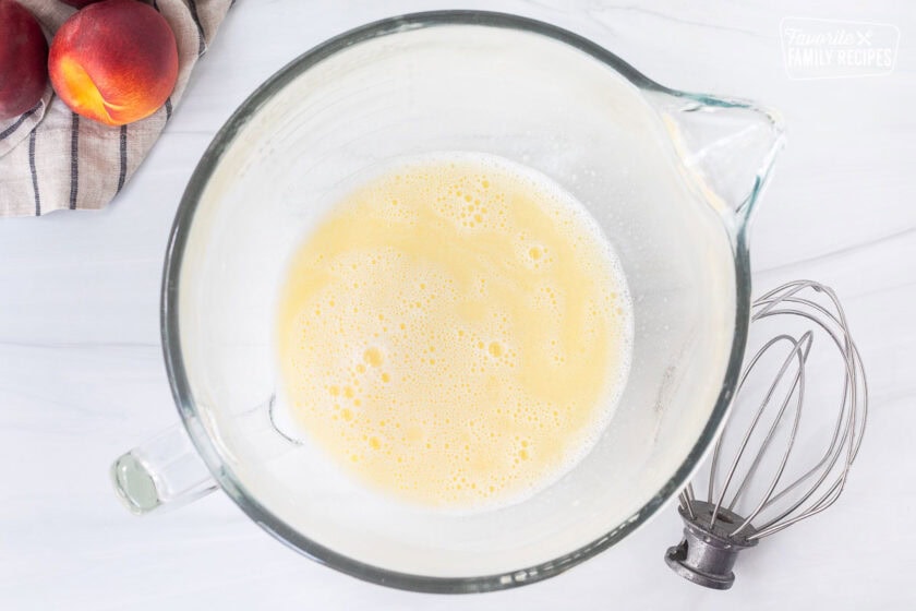 Glass mixing bowl with warm milk and butter. Whisk on the side.