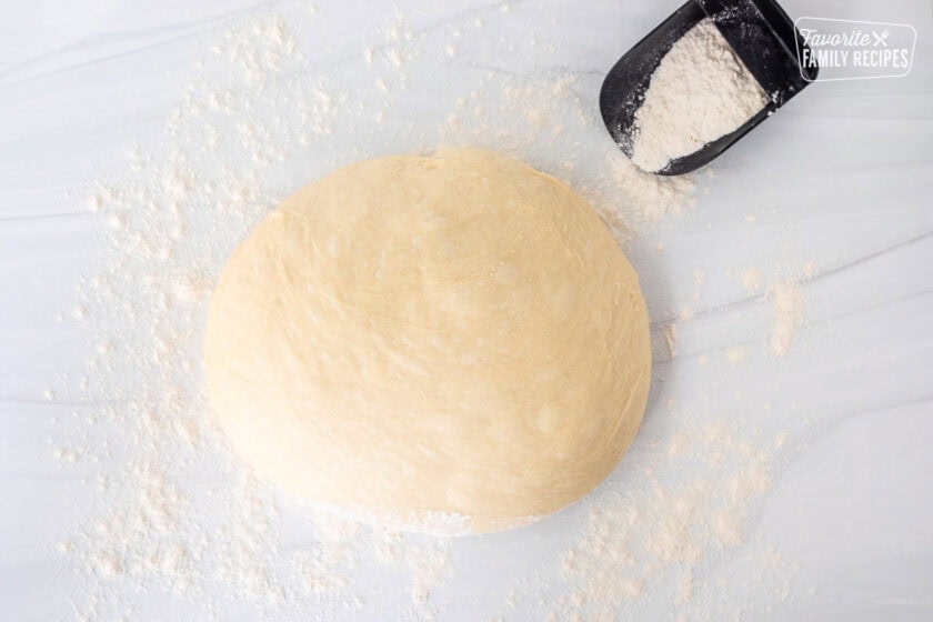 Cinnamon roll dough on a floured surface with extra flour on the side.