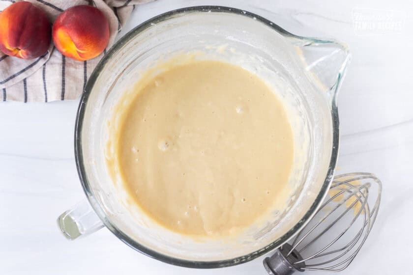 Glass mixing bowl with eggs and flour added to milk. Whisk on the side.