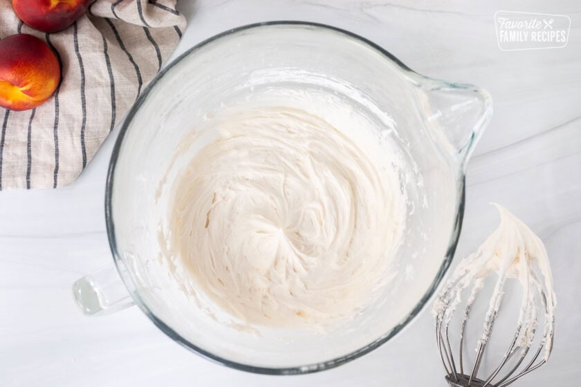 Glass mixing bowl with frosting and whisk on the side.