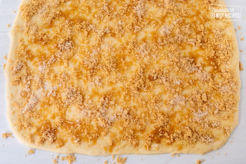 Rolled out cinnamon roll dough sprinkled with butter, sugars and cinnamon.