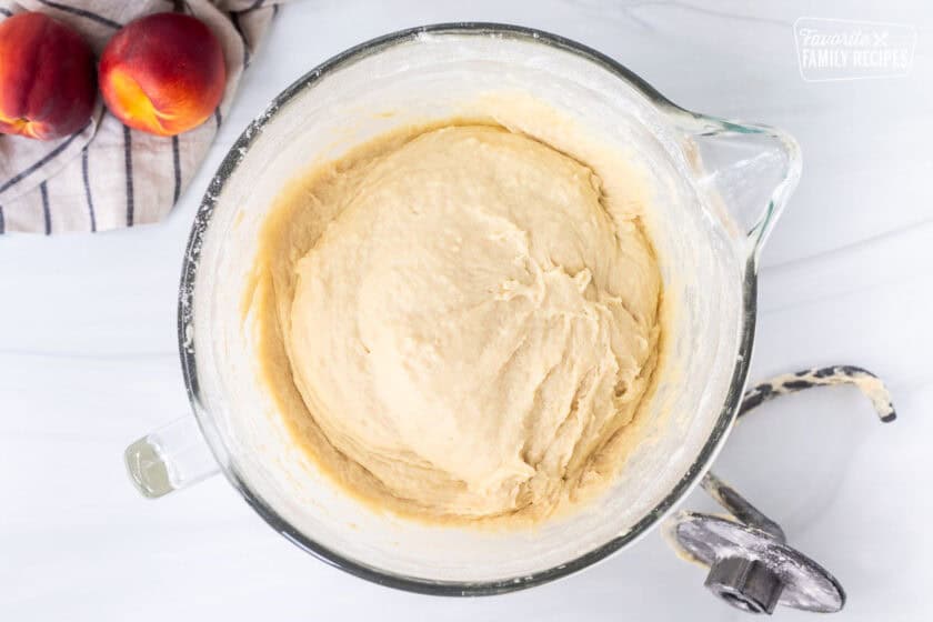 Glass mixing bowl with cinnamon roll dough and bread hook on the side.