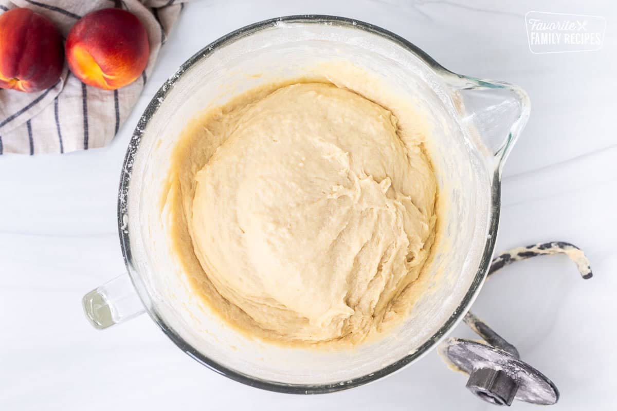 Glass mixing bowl with cinnamon roll dough and bread hook on the side.