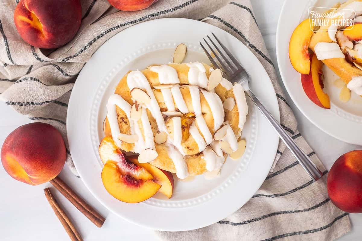 Peach cinnamon roll on a plate with sliced peaches and fork on the side.