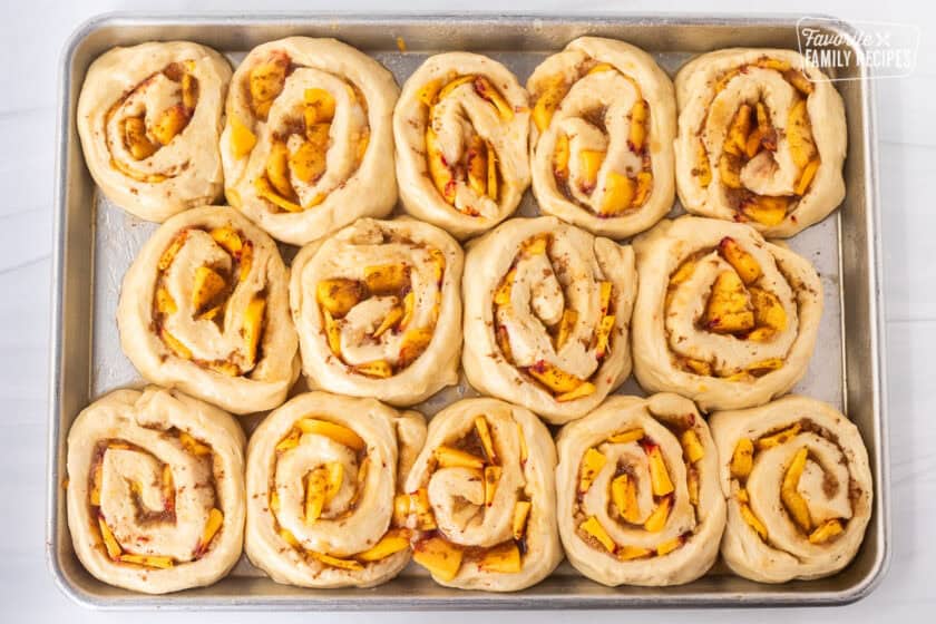Sheet pan with rolled peach cinnamon rolls unbaked.
