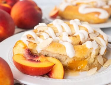 Peach cinnamon roll on a plate with sliced peaches and fork on the side.