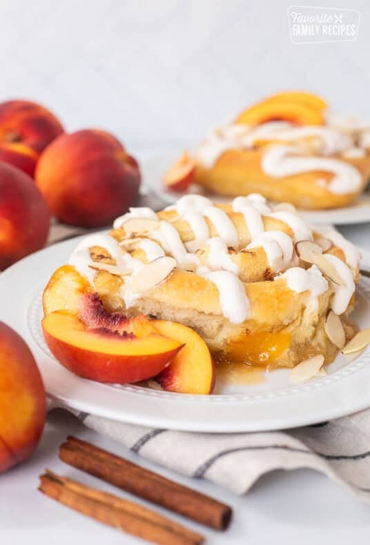 Peach cinnamon roll on a plate with sliced peaches and fork on the side.