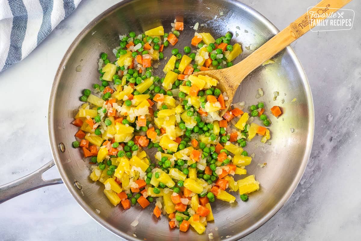 Skillet with onion, pineapple and vegetables with a wooden spoon.