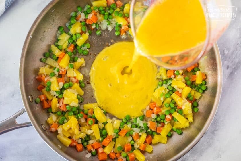 Pouring egg into skillet with pineapple, and veggies around the edges.