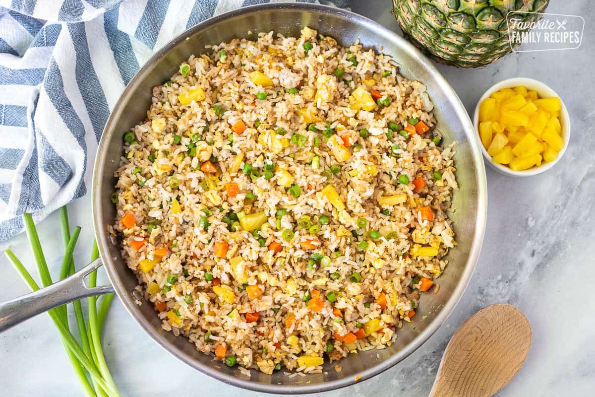 Skillet of pineapple fried rice with rice, pineapple, carrots, peas and green onion.