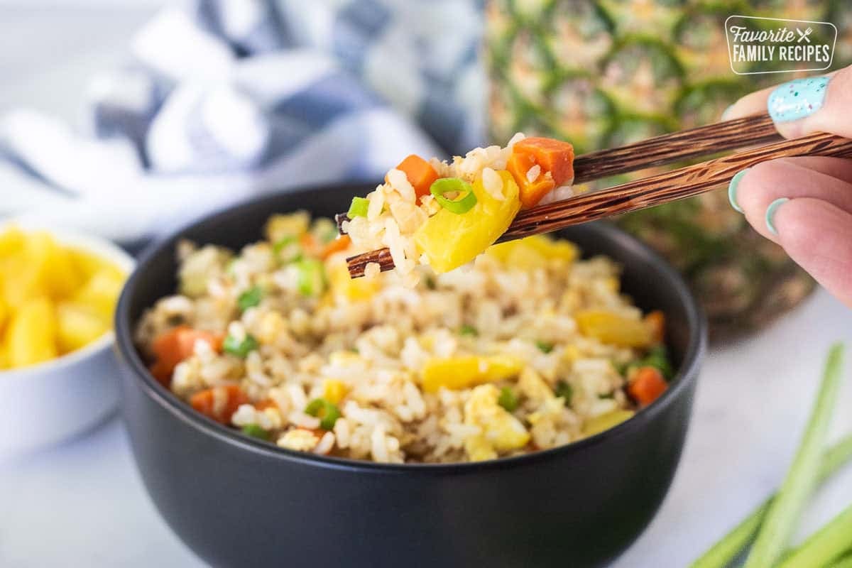 Chopsticks holding up pineapple fried rice with green onion.
