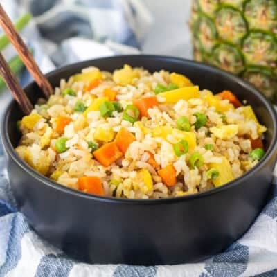 Bowl of pineapple fried rice with pineapple, carrots, peas and green onion.