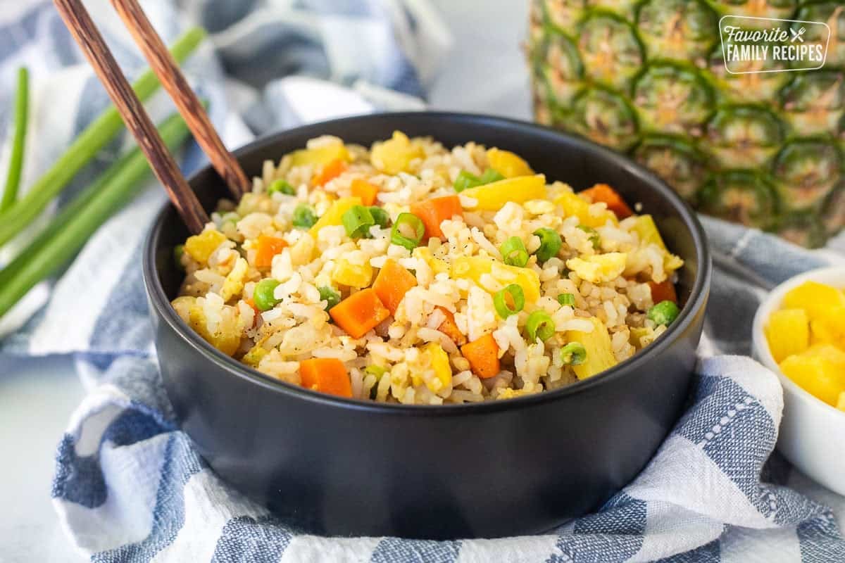 Bowl of pineapple fried rice with pineapple, carrots, peas and green onion.