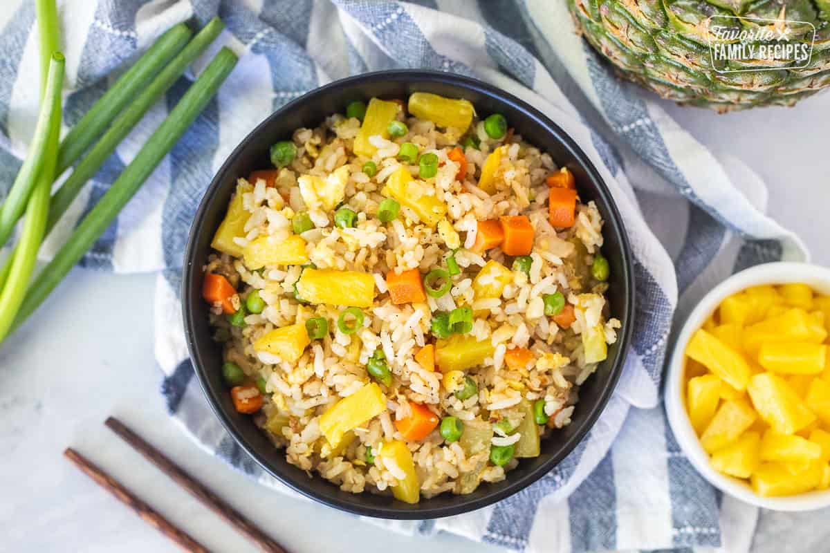 Bowl of pineapple fried rice with pineapple, carrots, peas and green onion.