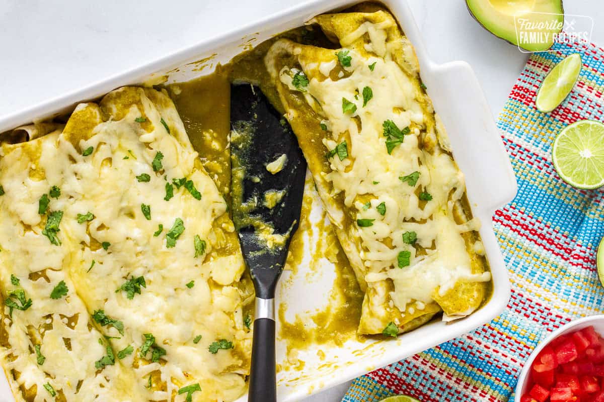 Baking dish with green sauce spinach enchiladas and spatula.