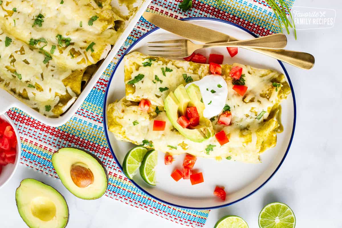 Plate with two green sauce spinach enchiladas garnished with sliced avocado, sour cream, tomatoes and cilantro.