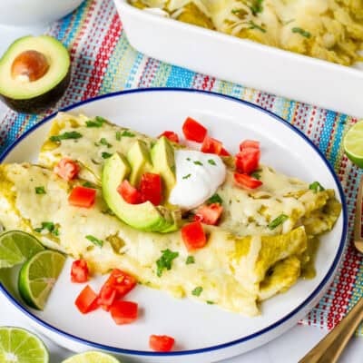 Plate with two green sauce spinach enchiladas garnished with sliced avocado, sour cream, tomatoes and cilantro.