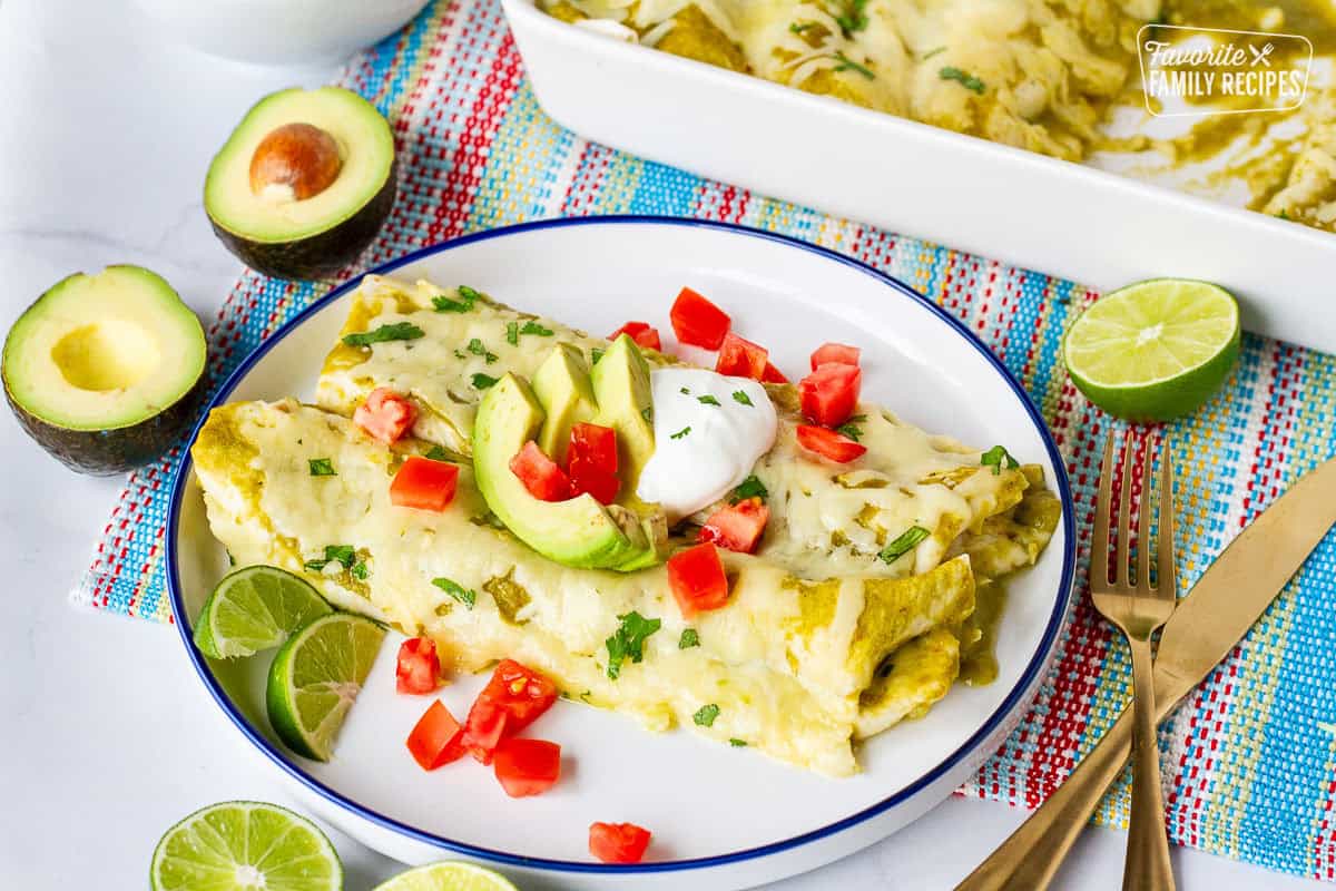 Plate with two green sauce spinach enchiladas garnished with sliced avocado, sour cream, tomatoes and cilantro.