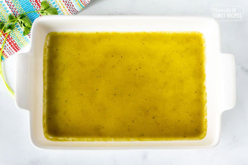 Baking dish with green enchilada sauce on the bottom.