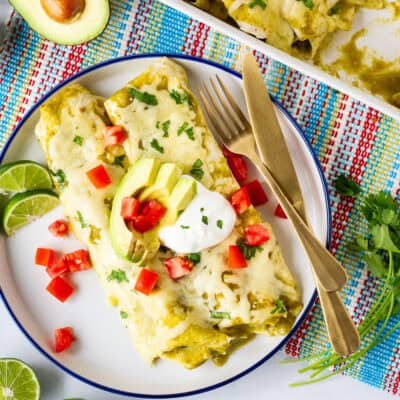 Plate with two green sauce spinach enchiladas garnished with sliced avocado, sour cream, tomatoes and cilantro.