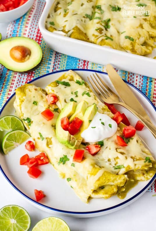 Plate with two green sauce spinach enchiladas garnished with sliced avocado, sour cream, tomatoes and cilantro.