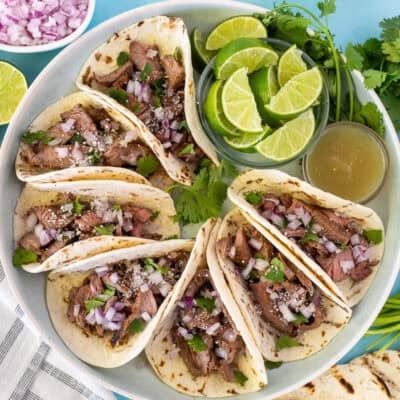Street tacos arranged on a plate garnished with cilantro, red onion and cojita cheese.