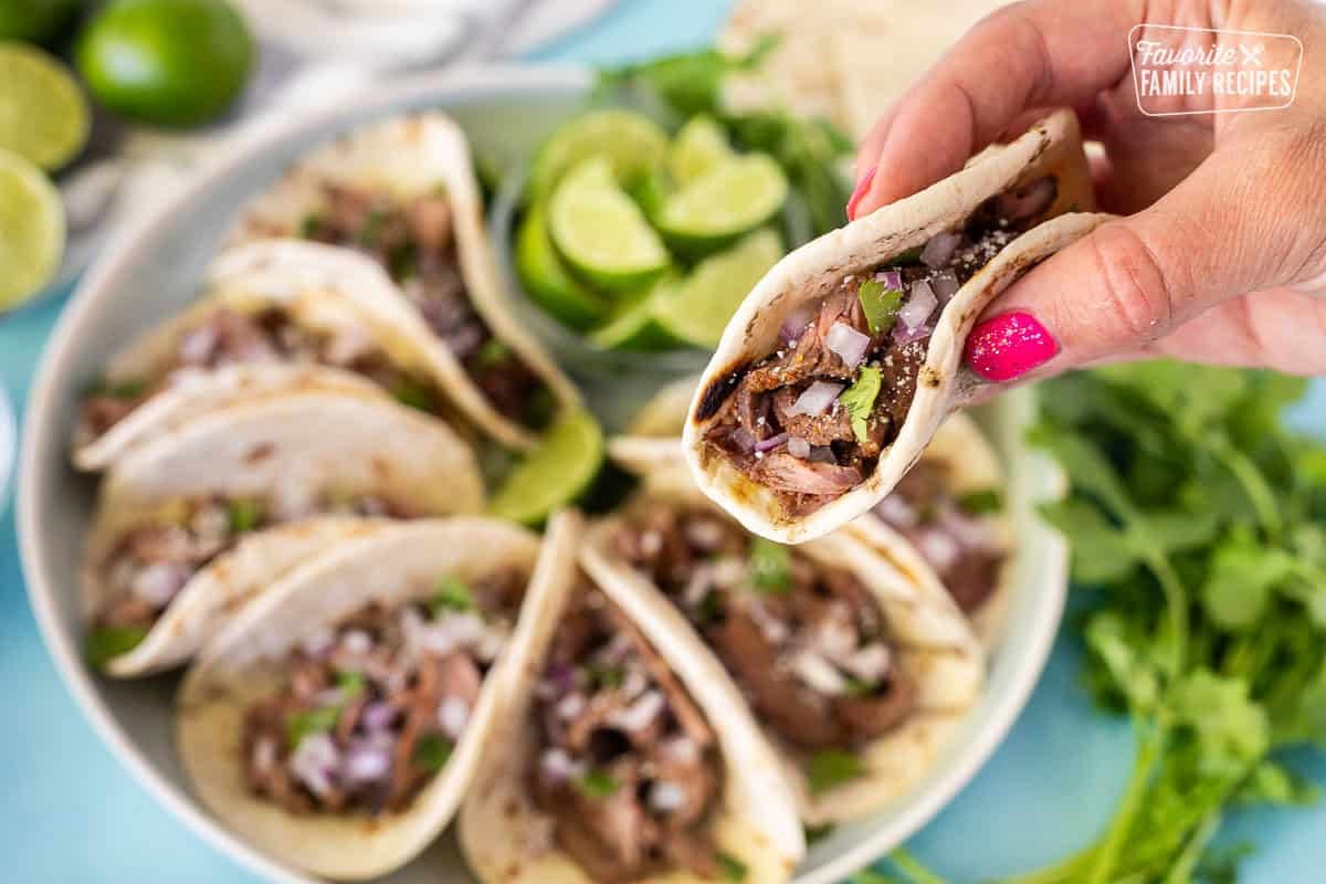 Hand holding a street tacos with steak, cilantro, red onion and cojita cheese.
