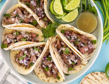 Street tacos arranged on a plate garnished with cilantro, red onion and cojita cheese.