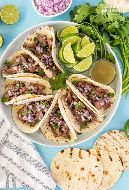 Street tacos arranged on a plate garnished with cilantro, red onion and cojita cheese.