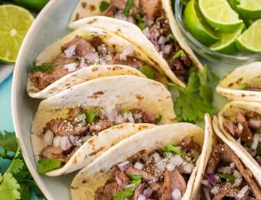 Street tacos arranged on a plate garnished with cilantro, red onion and cojita cheese.