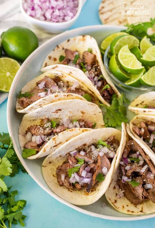Street tacos arranged on a plate garnished with cilantro, red onion and cojita cheese.