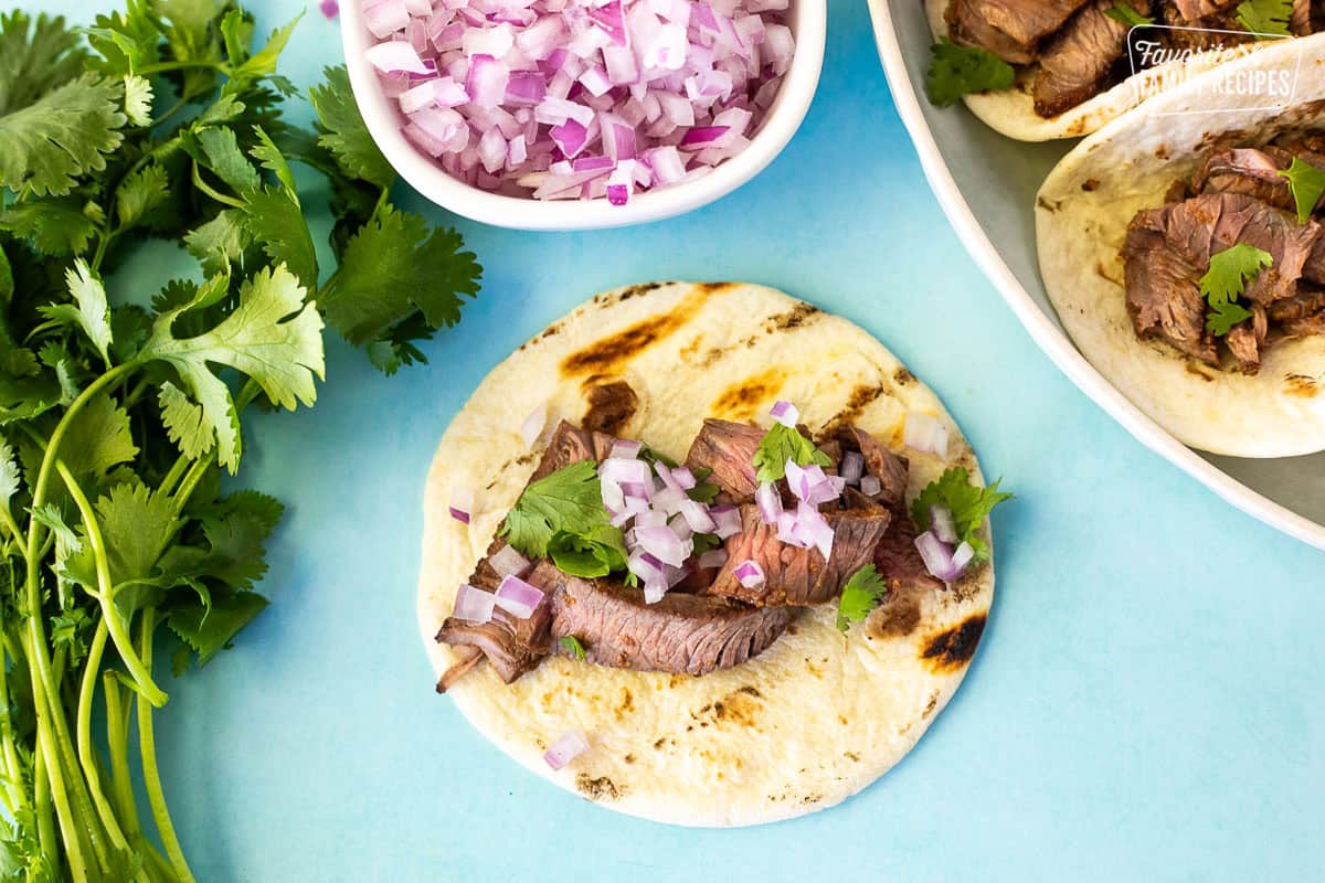 Small flour tortilla with sliced steak, cilantro and red onion on top.