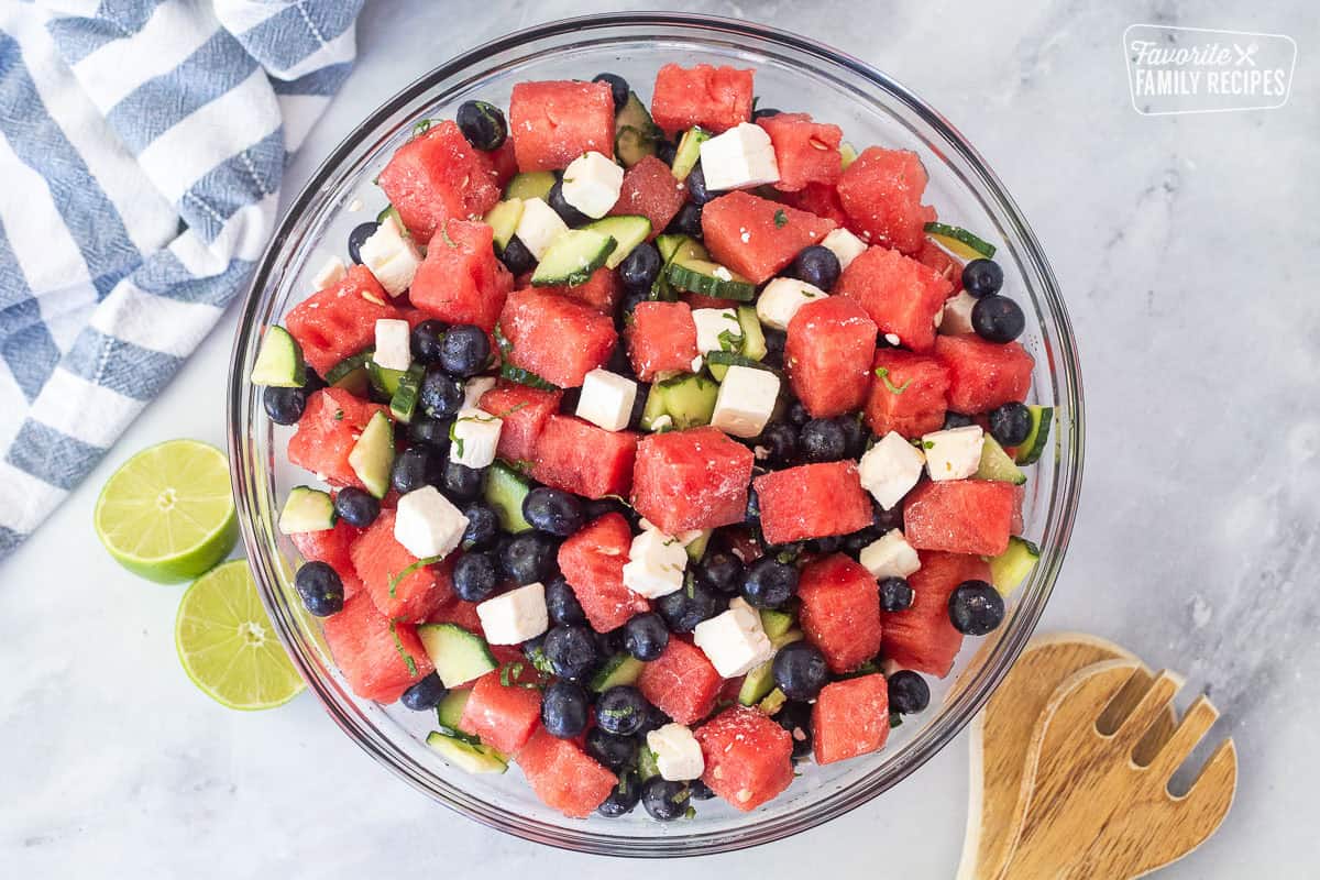 Watermelon feta salad in a glass bowl with watermelon, blueberries, feta cheese, cucumbers, milt, basil, salt and lime juice.