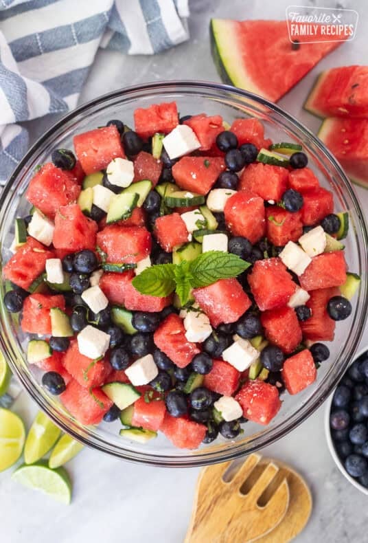 Watermelon feta salad in a glass bowl with watermelon, blueberries, feta cheese, cucumbers, milt, basil, salt and lime juice. Garnished with mint leaves.