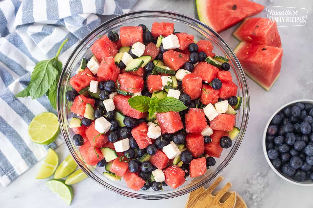Watermelon feta salad in a glass bowl with watermelon, blueberries, feta cheese, cucumbers, milt, basil, salt and lime juice. Garnished with mint leaves.