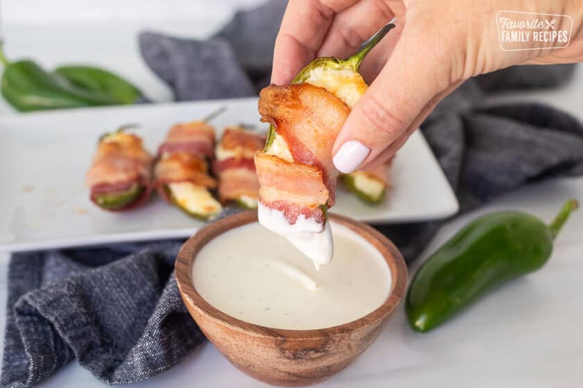 Hand holding a bacon wrapped jalapeño popper dipped in Ranch.