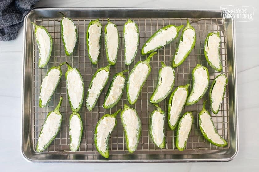 Filling jalapeños with cheese mixture on a sheet pan with wire rack.