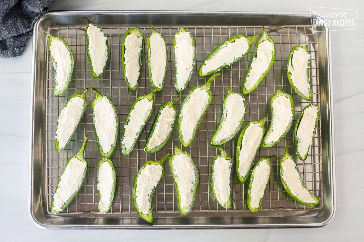 Filling jalapeños with cheese mixture on a sheet pan with wire rack.
