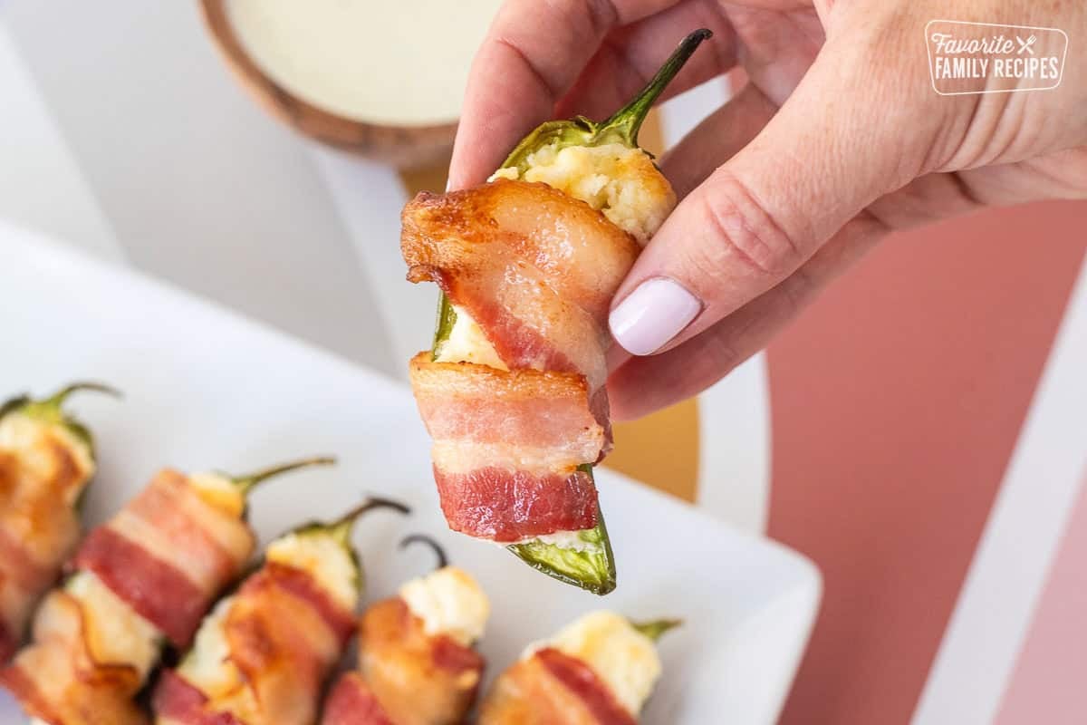 Hand holding a bacon wrapped jalapeño popper.