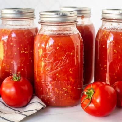 Canned diced tomatoes in jars with fresh tomatoes on the side.