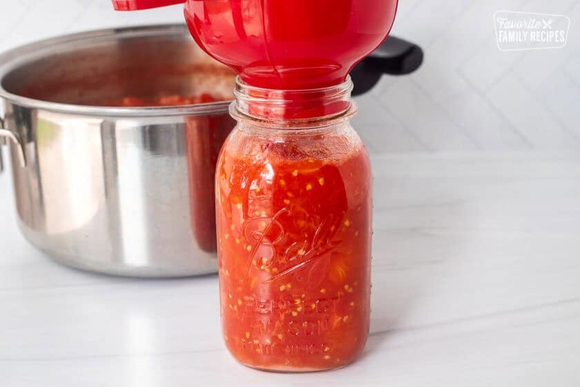 Canning jar with dice tomatoes filled to the top and a canning funnel on top.