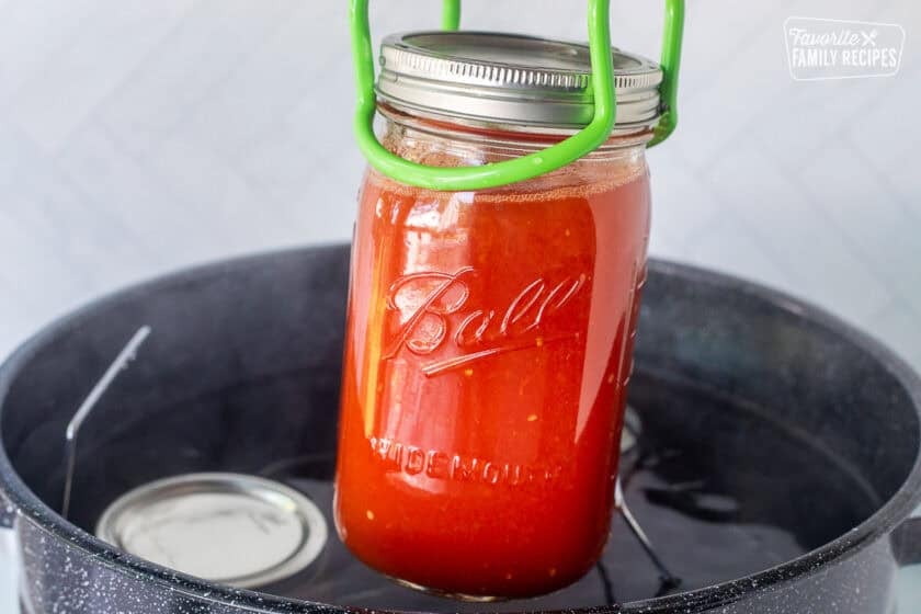 Lifting hot canning jar of tomato juice out of a canning pot.