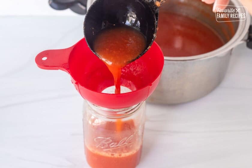 Pouring tomato juice into the canning jar using a canning funnel and ladle.