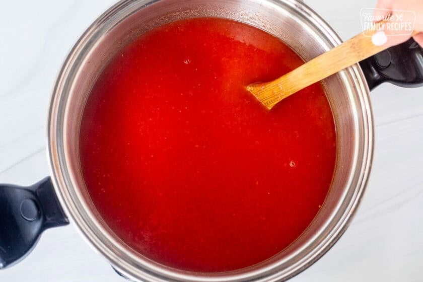 Tomato juice in a large pot stirred with a wooden spoon.