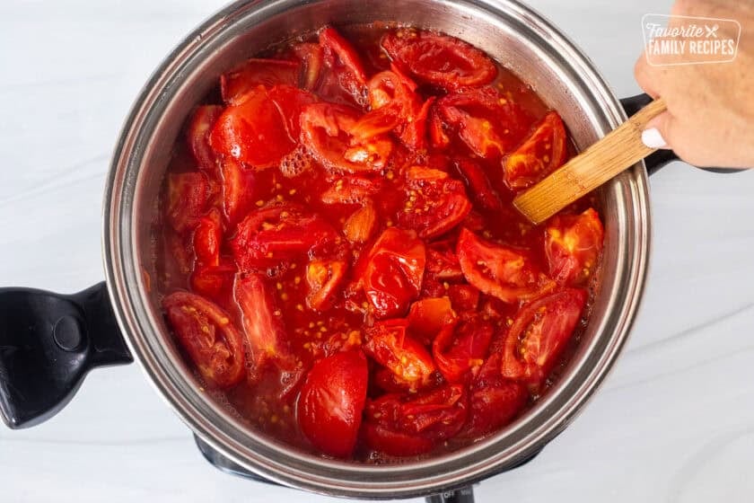 Stirring large pot of cut tomatoes over an electric skillet.