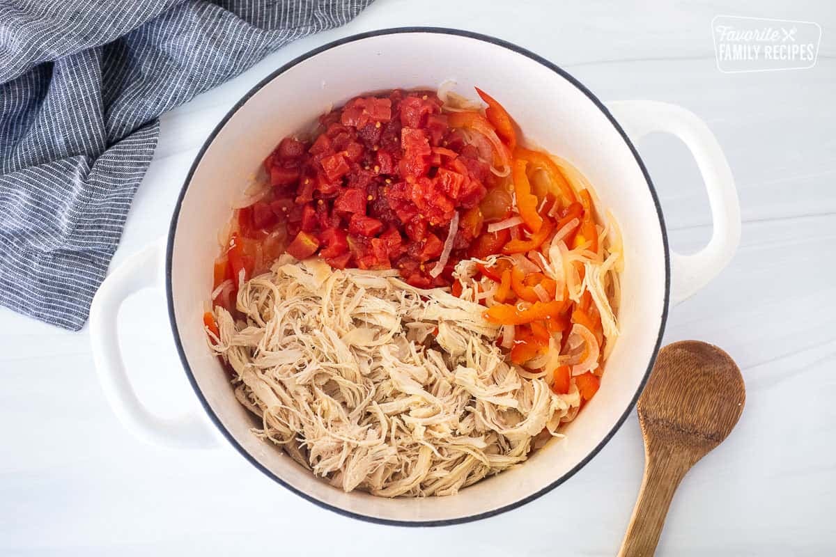 Dutch oven with cooked peppers, onions, shredded chicken and rotel tomatoes. Wooden spoon on the side.